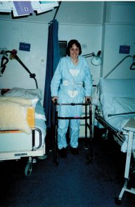 Photo of me, standing holding on to a walking frame, I have t shaped back brace and an ankle foot orthotic