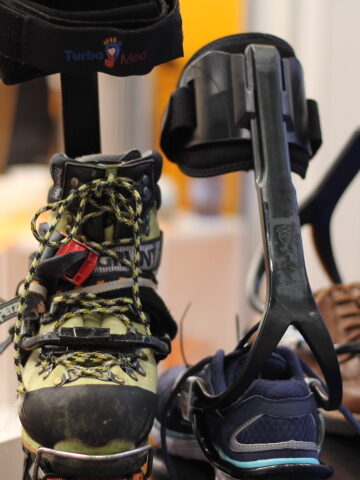 Mountain climbing boot with a crampon attached next to a shoe. Both have a turbomed ankle foot orthotic attached